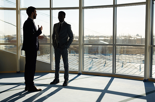 Communicating businessmen standing by office window on sunny day