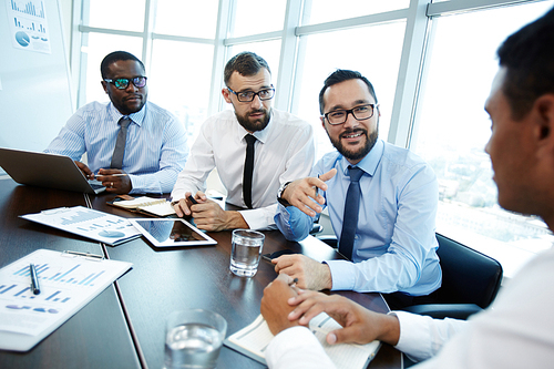 Three bearded employees in eyeglasses conducting negotiations with their business partner while sitting in modern meeting room