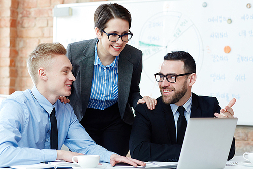 Happy men discussing online data with female colleague near by