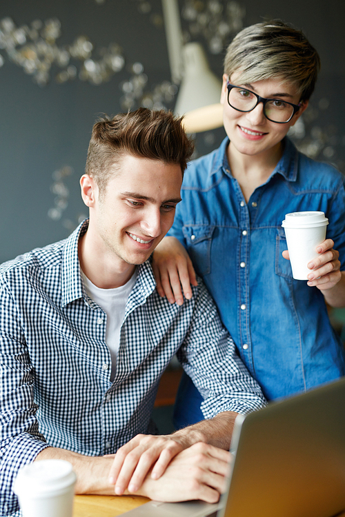 Portrait of creative business colleagues dressed in smart casual, smiling cheerfully while working with laptop at cafe table during coffee break