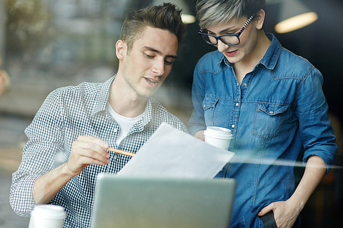 Informal business meeting in coffeehouse: young handsome man sitting at table and discussing new contract terms with his business partner before signing it, view through window