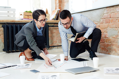 Female economist pointing at paper on the floor while explaining data to co-worker