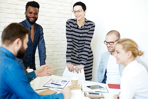 Group of creative designers looking at their bearded colleague with interest while he presenting them his ideas concerning joint project in modern boardroom