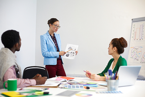 Young woman pointing at financial chart on paper while explaining data to colleagues