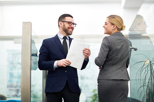 Happy office workers looking at one another while talking in aisle