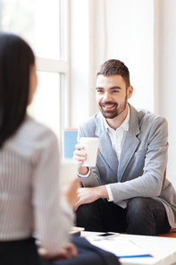 Happy man with drink listening to his colleague during coffee-break