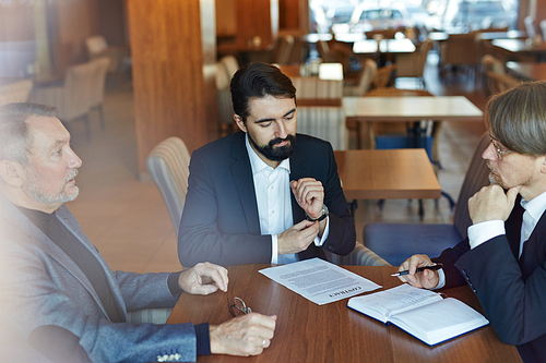 Three male business partners gathered together in spacious cafe and discussing necessary changes in contract, waist-up portrait