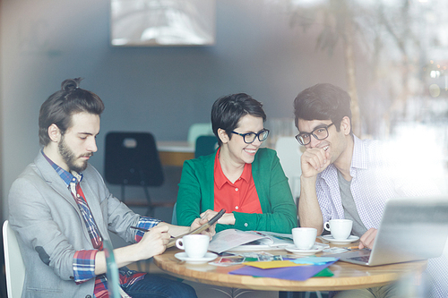 Group of young creative people wearing business casual clothes smiling at work meeting in cafe