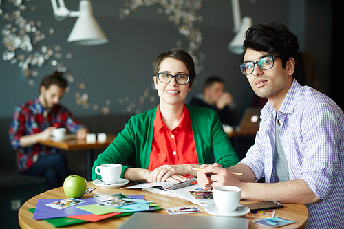 Portrait of two casual young colleagues man and woman  wearing glasses, discussing work at meeting in cafe and smiling, 