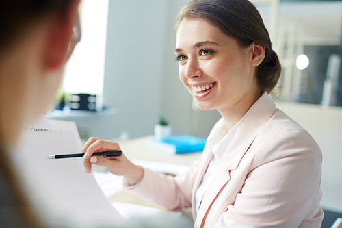 Smiling accountant pointing at financial document in her hand while talking to colleague