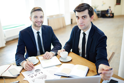 Modern traders sitting by workplace and discussing data