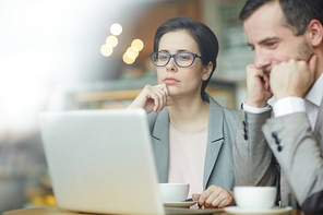 Pensive employees reading online information in laptop