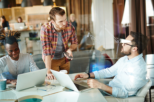 Young bearded businessman in casualwear listening to his colleague with attention while having brainstorm in glass boardroom