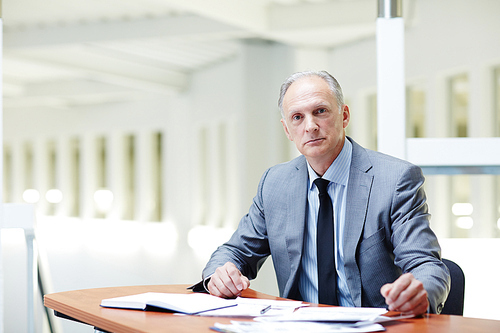 Senior boss in formalwear sitting by workplace in office