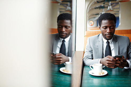 Elegant man sitting in steamship cafe and texting in smartphone