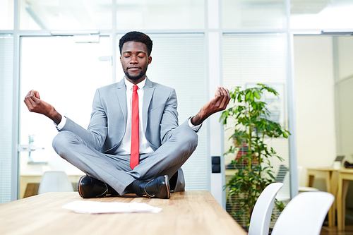 African-american businessman in corporate attire meditating on desk in boardroom