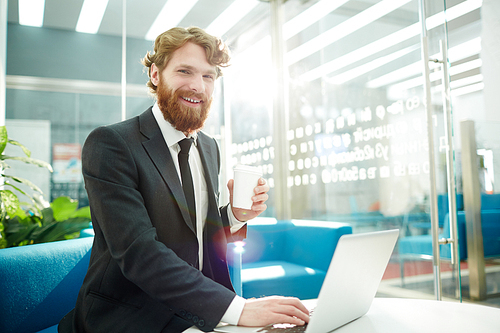 Successful employer with drink looking through online resumes of applicants in office