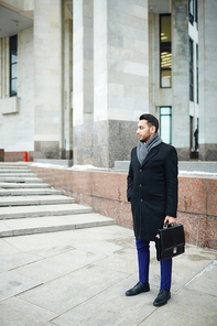 Young handsome Middle-Eastern man standing among modern city architecture