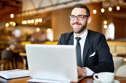 Posh businessman in elegant suit sitting in front of laptop and searching in the net