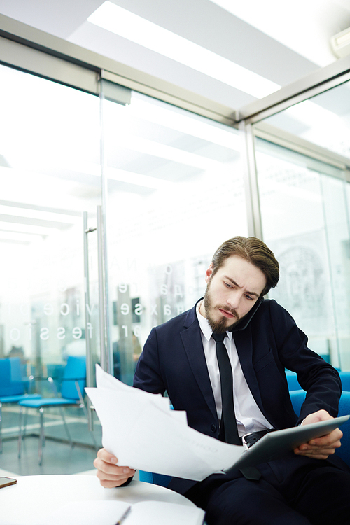 Financial director with touchpad and documents speaking on cellphone in office