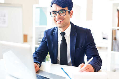 Successful businessman sitting by workplace in front of laptop at work