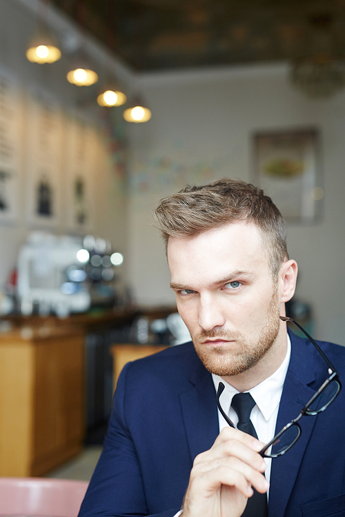 Serious young man with eyeglasses relaxing in cafe