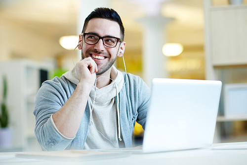 Portrait of modern smiling man listening to music from laptop in office