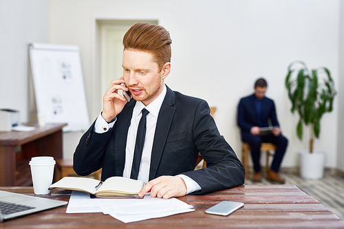 Portrait of young red haired man in business suit working in office answering phone calls