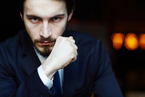 Head and shoulders portrait of handsome bearded man wearing elegant business suit, looking strongly at camera with powerful hand gesture