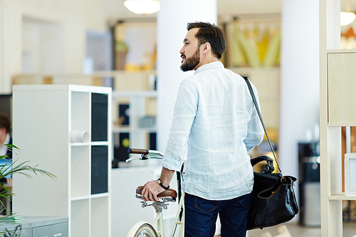 Back view portrait of casual Asian businessman taking bicycle to work in modern creative office