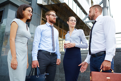 Group of young successful business people chatting outside modern office building during break