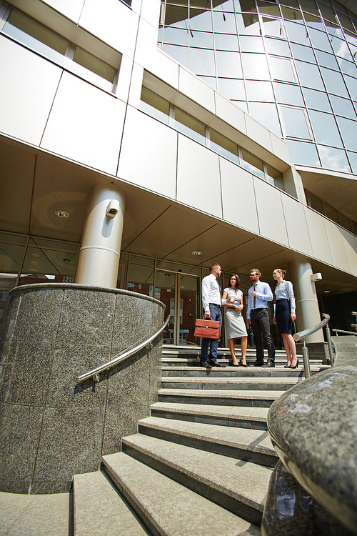 Group of business people standing on steps of modern office building with glass fronts and winding stone stairs