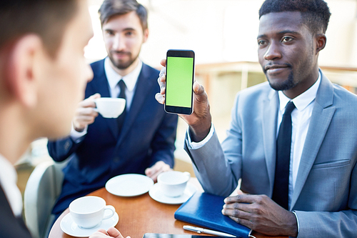 Confident employee showing touchscreen of smartphone to colleague