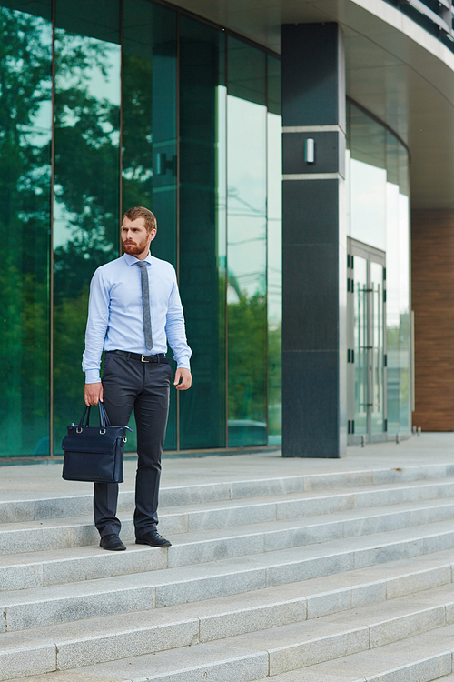 Portrait of handsome young man standing on steps outside modern office building with glass fronts