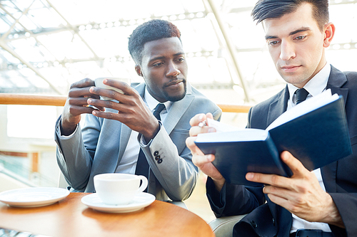 Businessmen reading notes in notebook while having tea