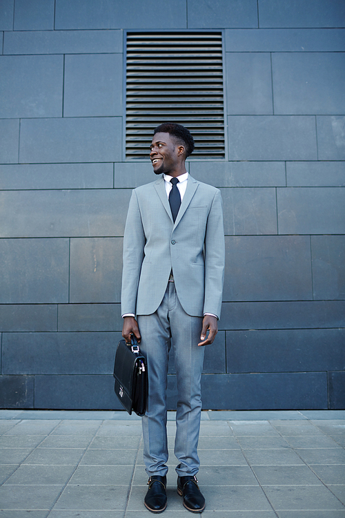 Happy African man in formalwear standing against wall of building