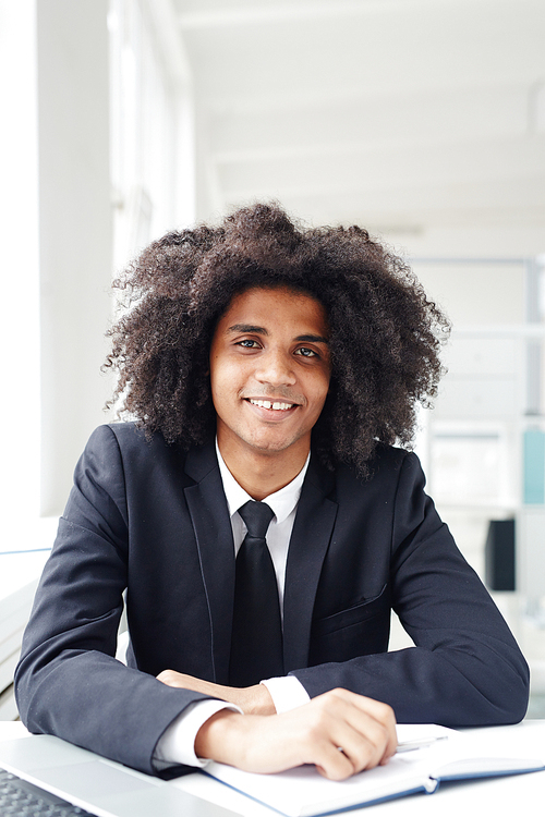 Hispanic businessman with open notebook sitting by workplace