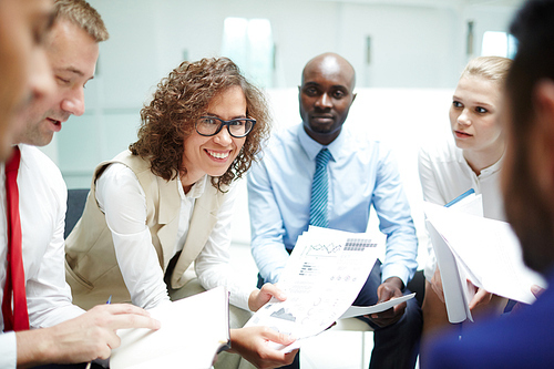 Happy economist with financial papers  while making report among her colleagues at meeting or seminar