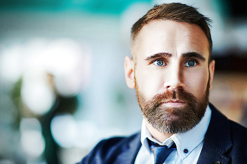 Portrait of mature bearded businessman wearing elegant formal suit looking away on blurred blue background in office