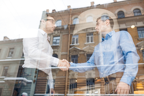 Side view portrait of two businessmen shaking hands after successful deal in meeting, shot from behind glass window