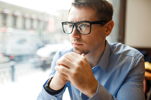 Portrait of thoughtful businessman sitting alone at table in cafe and looking out of window to streets