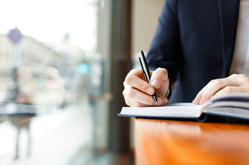 Closeup shot of unrecognizable businessman wearing formal suit making notes in planner scheduling for day