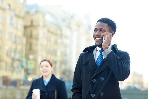 Portrait of two business colleagues in autumn street of city, African ?American man smiling cheerfully while talking by phone