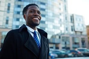 Portrait of excited African-American businessman smiling happily standing outside office building wearing winter coat