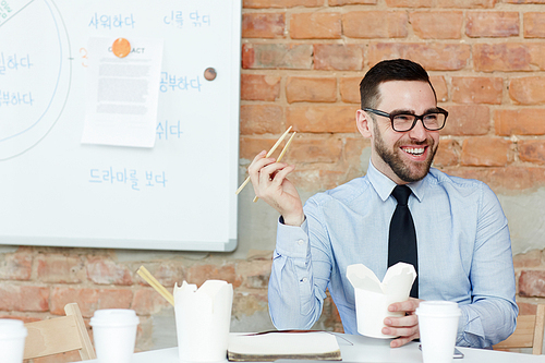 Happy trader with chopsticks eating take-away food from box