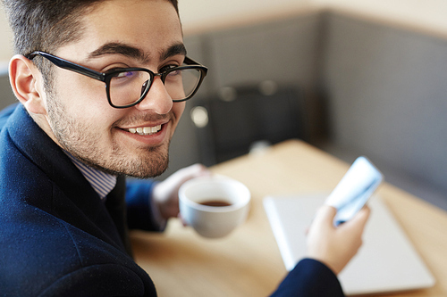 Cheerful businessman with cup of coffee and smartphone relaxing in cafe