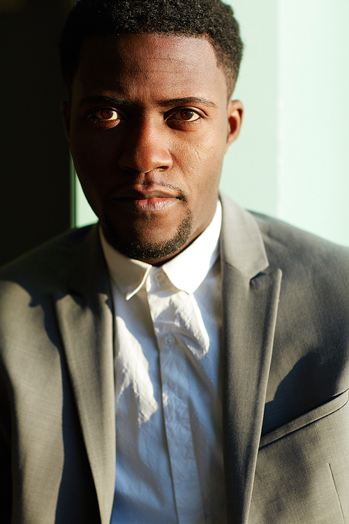 Business portrait of confident African-American man standing in shadow and 