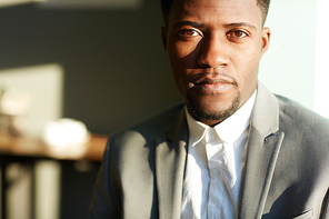 Head and shoulders portrait of confident young African-American businessman standing in office in bright sunlight and  with neutral expression