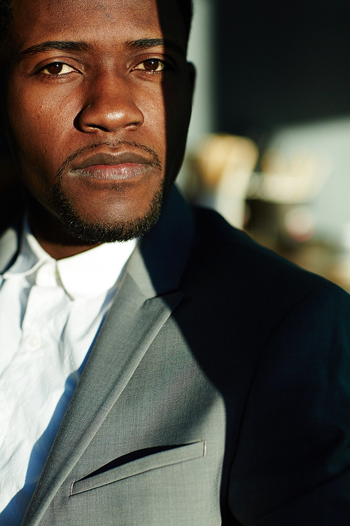 Business portrait of handsome African-American man standing in bright sunlight and  with serious expression