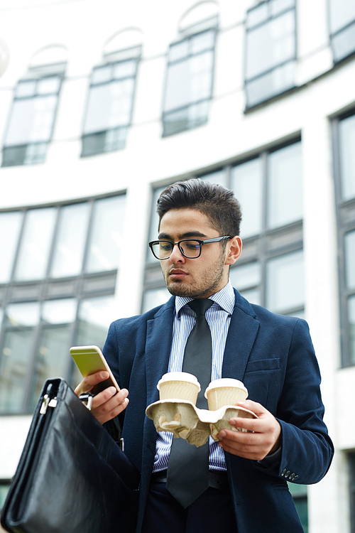 Young manager with briefcase and drinks texting outdoors